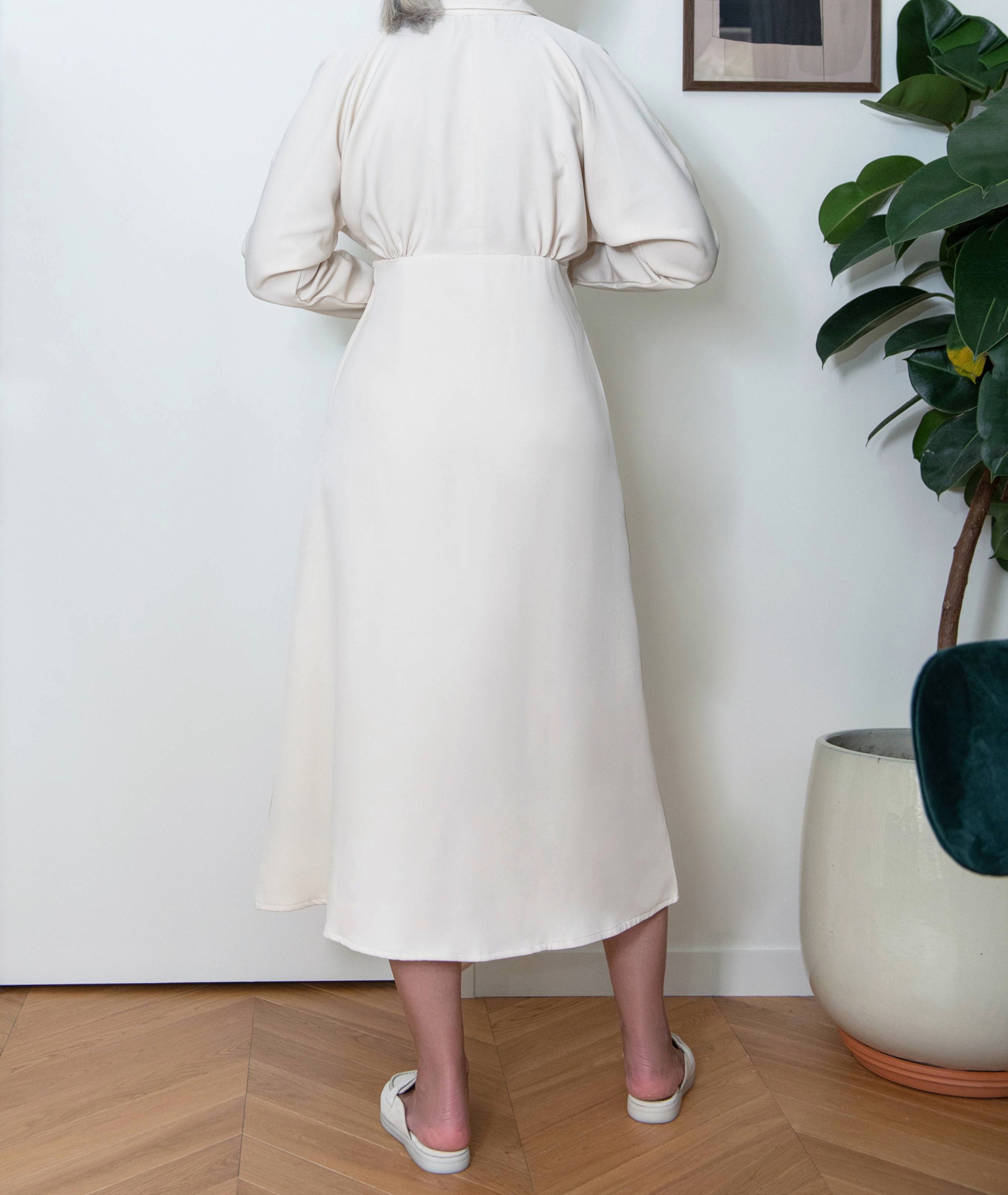 Alt text: Back view of Drift Midi Dress by IKKHO in ivory showing long sleeves and clean midi length silhouette